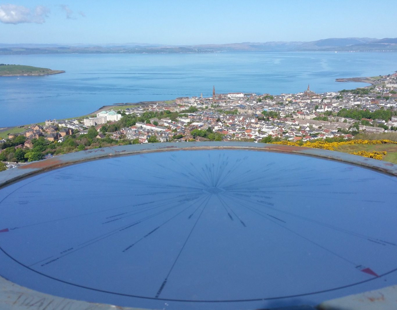 View of a town by the water, with a circular platform in the foreground and hills in the background.